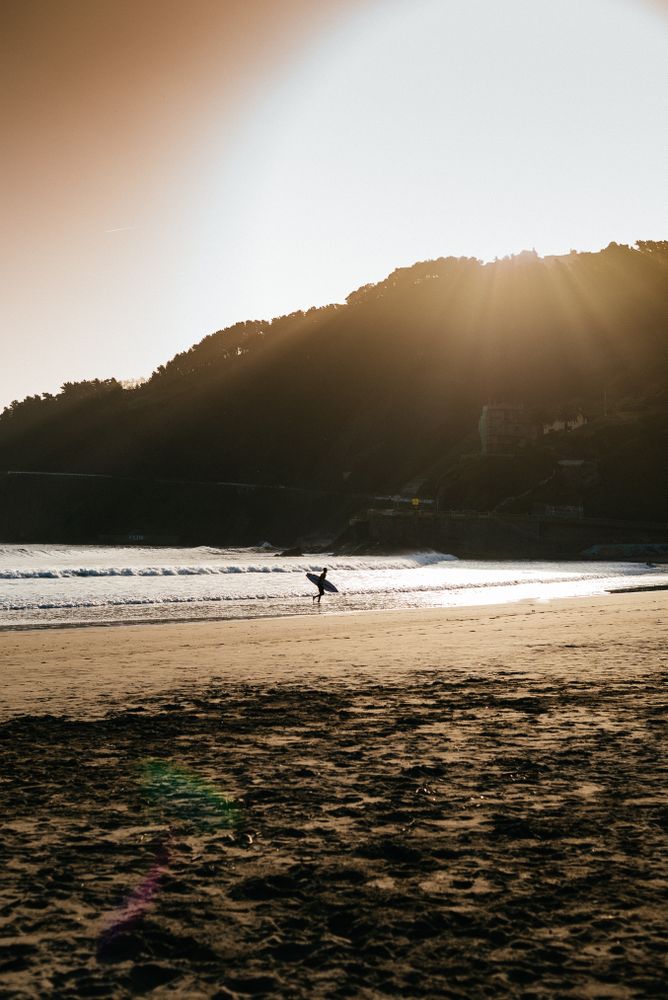 Person walking in the distance with surfboard near water's edge