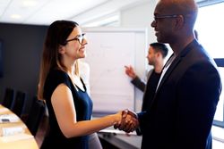 Male and female smiling and shaking hands in board room
