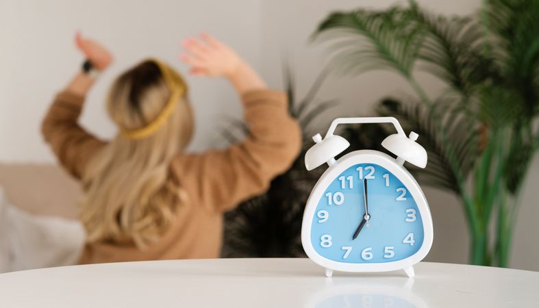 Alarm clock foreground, woman blurred in background.