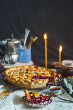 Slice of cherry pie on ceramic plate at candle-lit dinner table