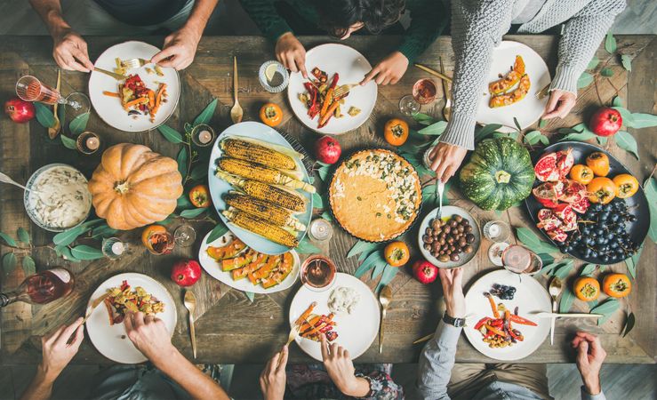 Group of people eating at festive vegetarian table setting with pie and corn
