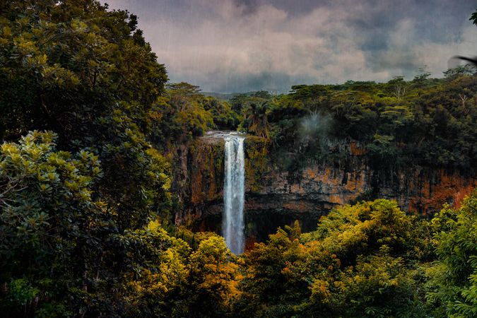 Waterfall surrounded by lush vegetation on cloudy day