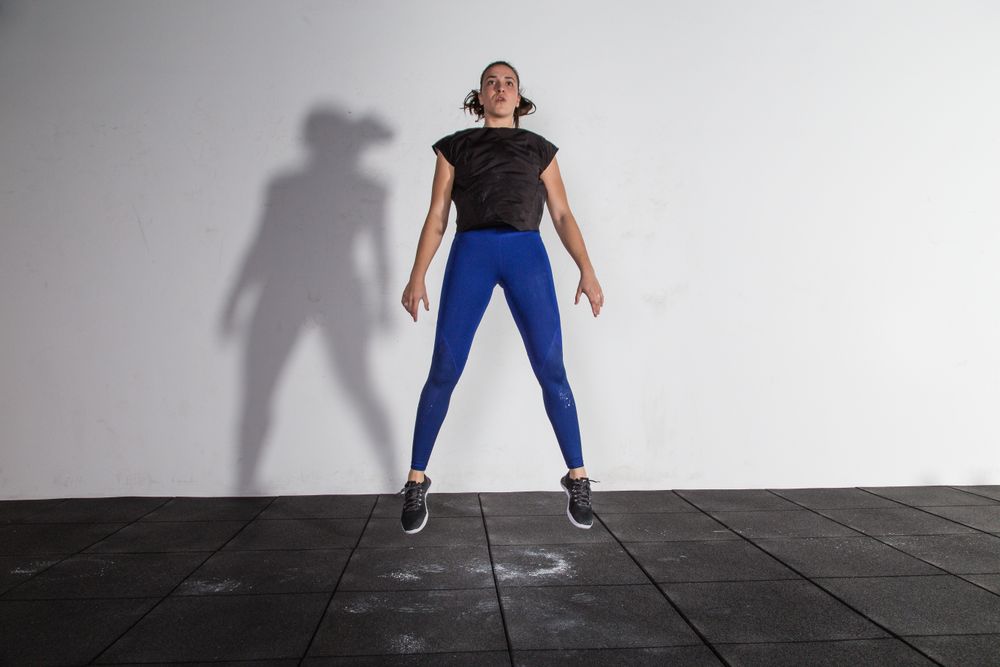 athletic young woman in sportswear doing squats and jumping in gym