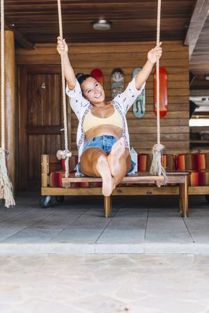Cheerful woman riding on swings on tropical terrace