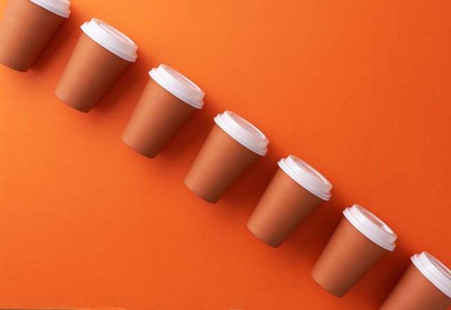 Diagonal row of disposable coffee cups on orange background