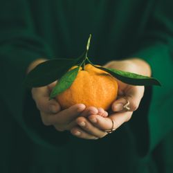Woman in green holding tangerine with both hands, square crop