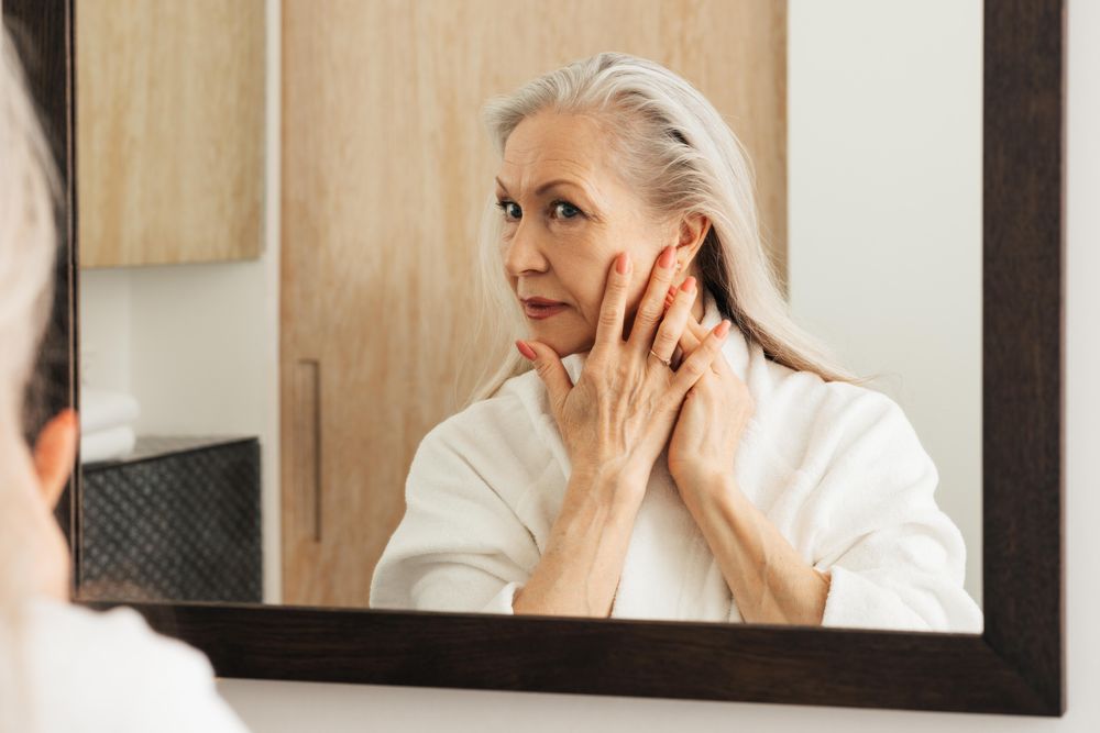 Female in bathrobe checking her skin in mirror