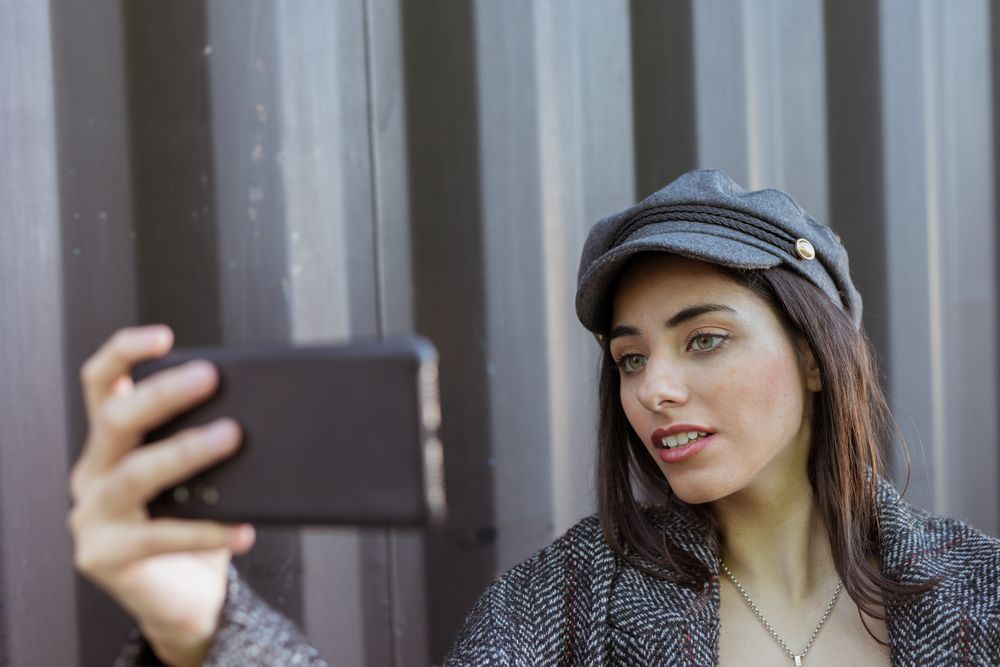 Charming Hispanic lady taking selfie near wall