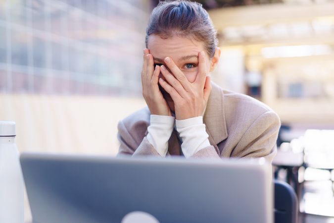 A stressed businesswoman is covering her face in front of her laptop while working