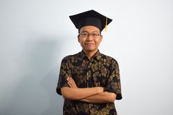 Proud graduate standing with arms crossed in studio shoot