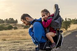 A father carrying his happy daughter in a child carrier backpack while hiking.