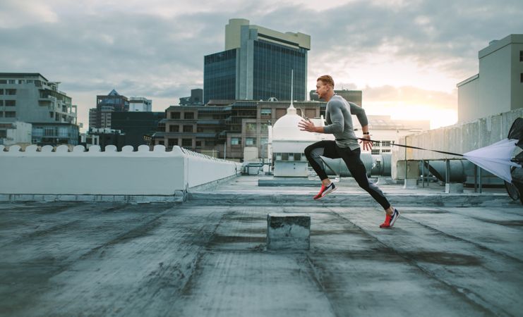 Side view of a fitness man running on rooftop using resistance parachute