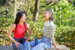 Two women sitting facing each other on outdoor bench in beautiful green park