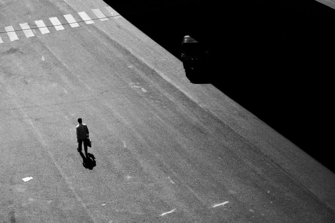 Grayscale photo of man walking on pedestrian lane