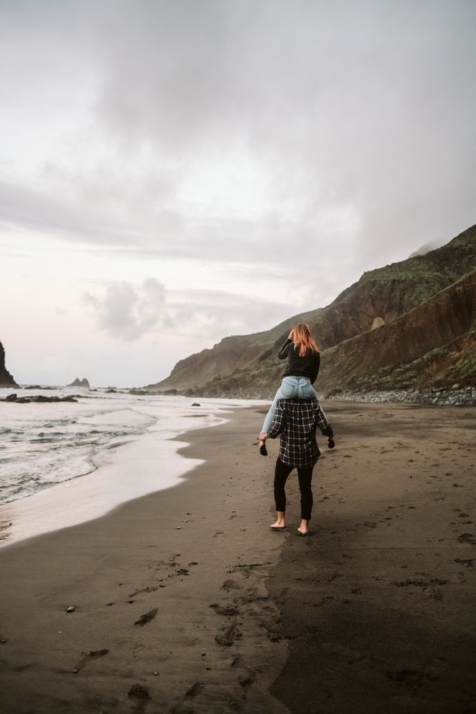Unrecognizable man carrying woman on shoulders near sea