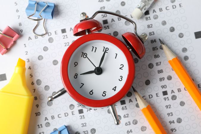 Top view of alarm clock and stationary on multiple-choice exam