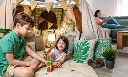 Little girl putting piece of stacking game while play with child and woman reading book on sofa