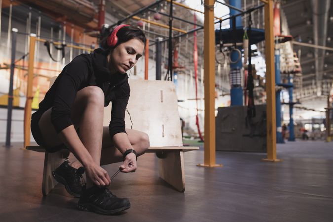 Smiling woman with headphones lacing shoe in gym