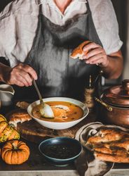 Woman in apron with spoon and bread eating soup in cozy kitchen