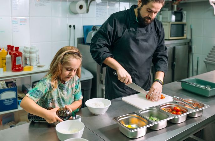 Chef preparing ingredients for healthy poke bowl with his daughter in restaurant kitchen