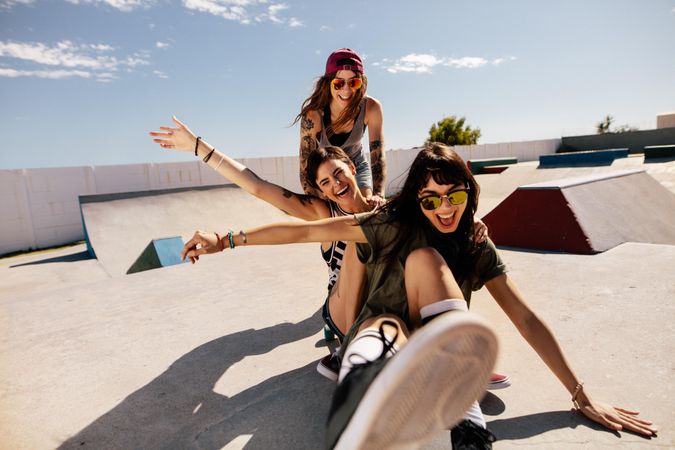 Two women sitting on skateboards while friend pushes them