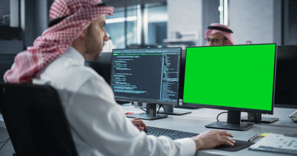 Arab Software Developer Working on Desktop Computer with Green Screen Mock Up Display.