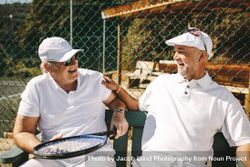 Mature men talking to each other sitting on bench during a game of tennis 4A6lRb