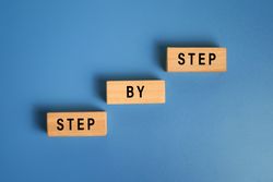 step by step word on wooden blocks staircase isolated on blue background. concept of success progress or career