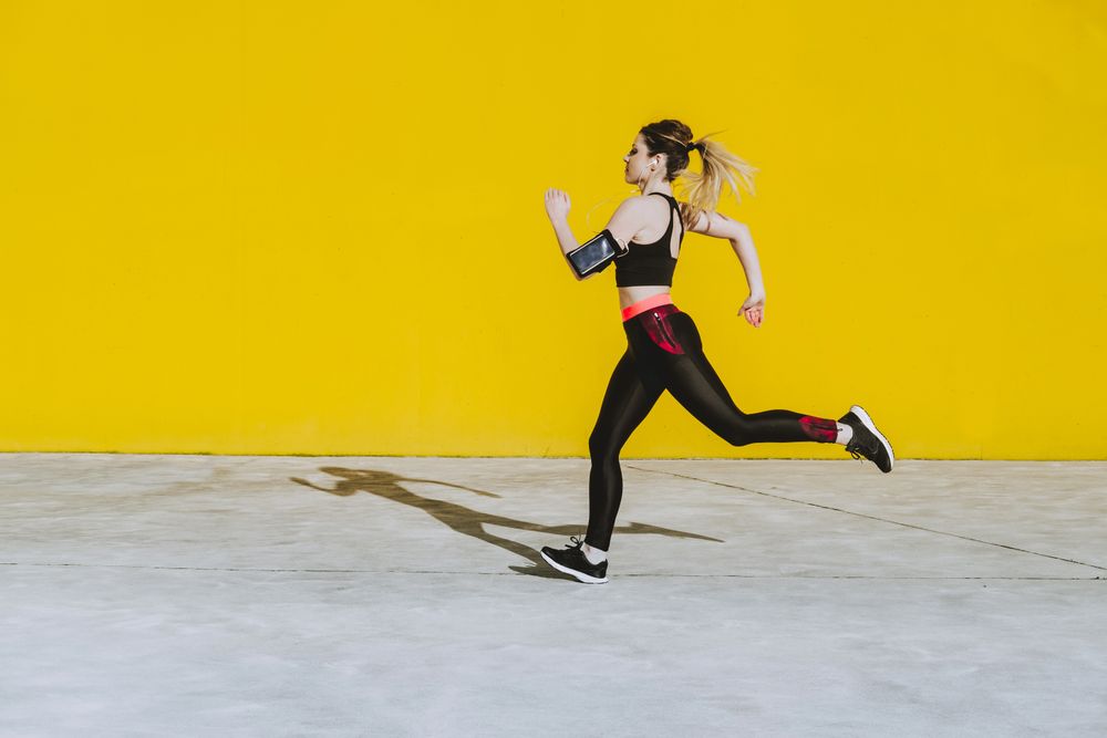 Woman with earphones running near wall