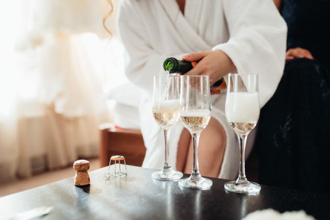 Woman in bathrobe pouring three glasses of sparkling wine