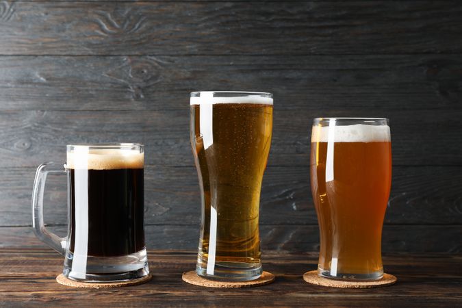 Different mugs with beer on wooden table, copy space