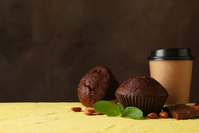 Composition with tasty muffins and paper cup on yellow table