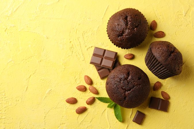 Delicious muffins, chocolate and almond on yellow background