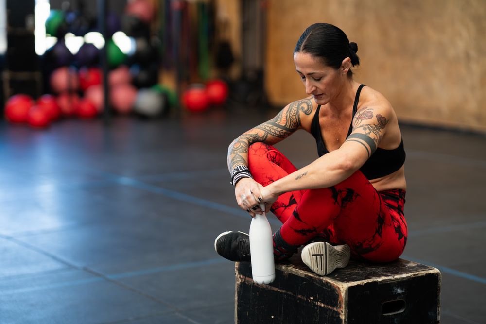 Tired woman looking down sitting on a box in gym