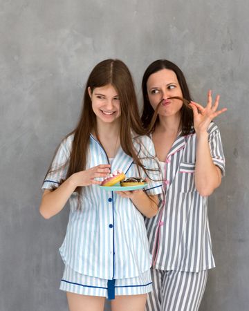 Mother and daughter in pajamas making funny faces with pastry.