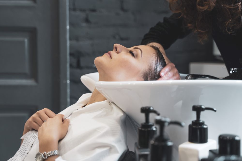 Stylist washing hair to young woman