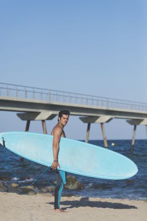 Male surfer with board standing on sunny beach