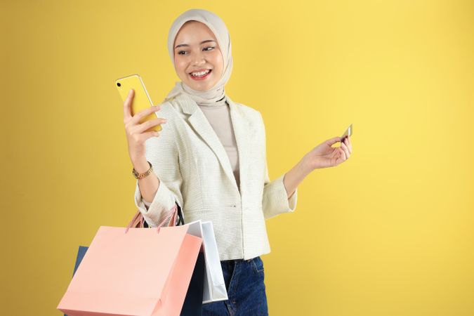 Asian Business Woman in Cream Suit and Hijab Holding a Smartphone and Credit Card