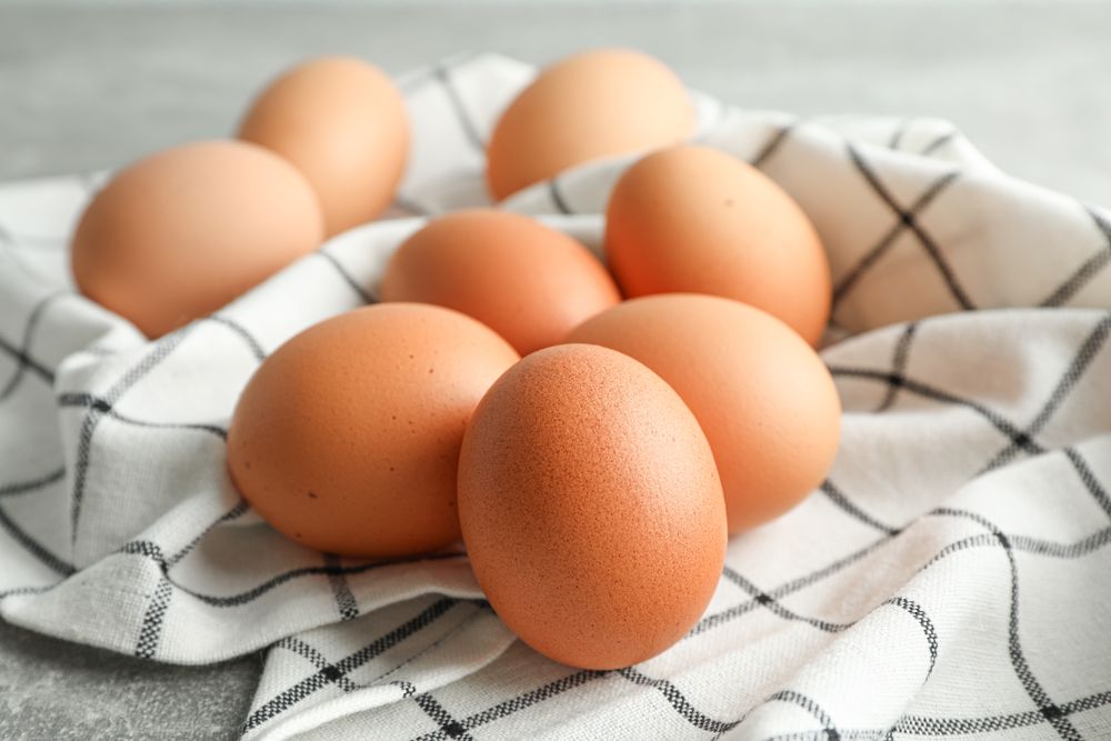 Brown chicken eggs in kitchen towel on grey background, space for text