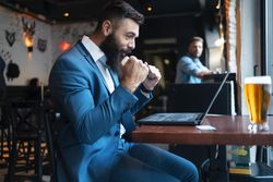 Man excited by game he’s watching on laptop in a pub