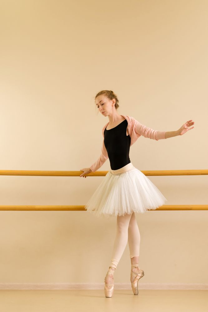 Ballet dancer balances on pointe, gently holding barre