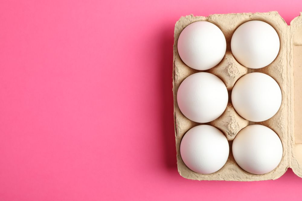 Chicken eggs in carton box on pink background, space for text