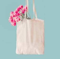 Pink tulips bunch in cotton shopping bag with copy space at light blue wall background. Springtime concept. Zero waste
