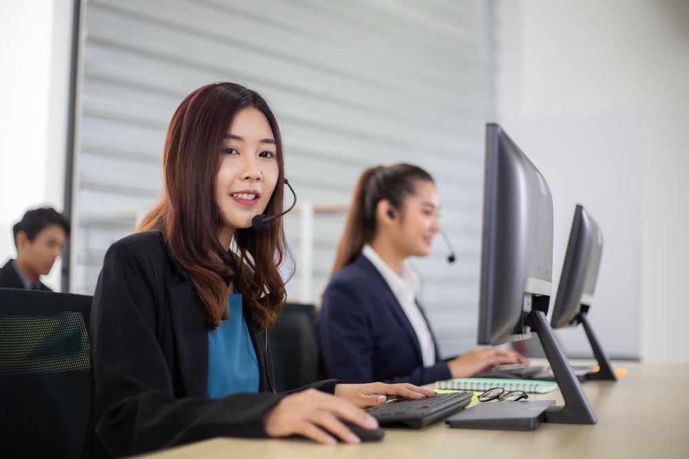 Call center with man and woman with headset sitting in office using computer