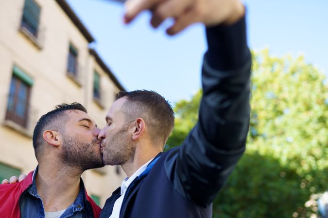 Two men kissing and taking selfie outside