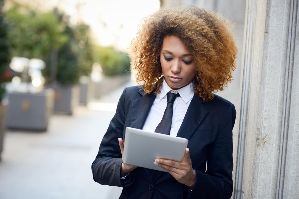 Serious female in suit standing outside checking her tablet