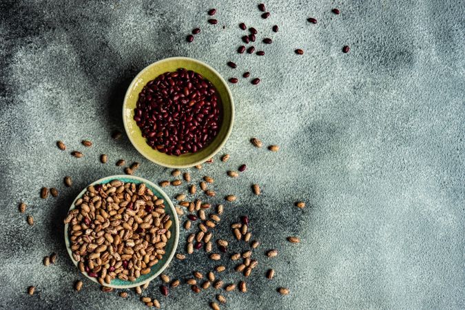 Top view of bowls of dried legumes from pantry on grey table with copy space