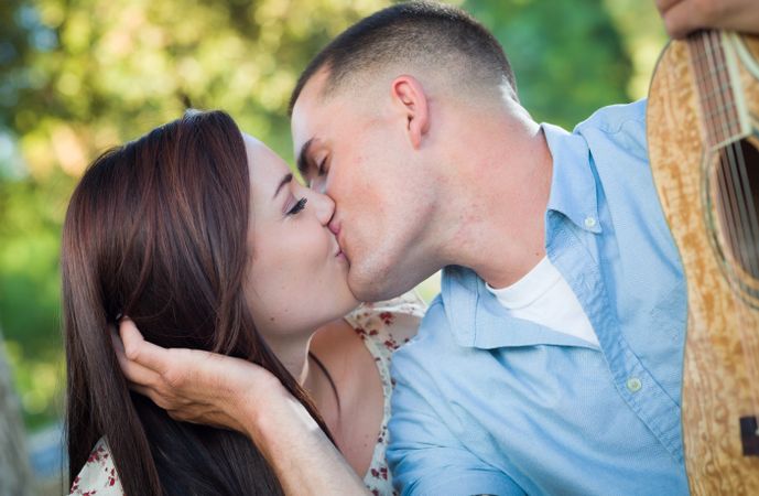 Young Adult Couple with Guitar Kissing in the Park