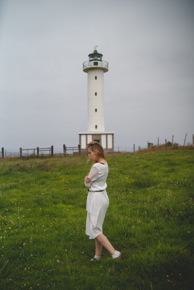Woman walking in green meadow near lighthouse