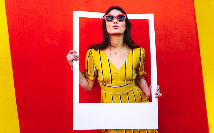 Young woman posing with photo frame against red and yellow colored wall